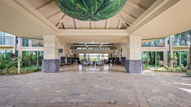 Un vestíbulo espacioso con piso de piedra, grandes columnas y un original adorno en forma de hoja verde en el techo.