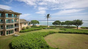 Un hotel con varios pisos, un jardín cuidado con setos y vistas al océano.