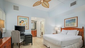 A hotel room with a bed, desk, chair, television, and artwork on the walls.