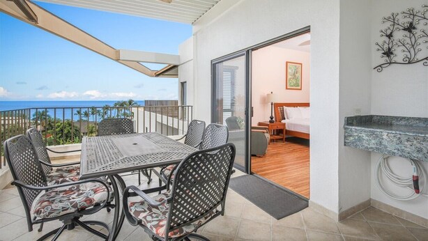 A balcony with a table and chairs, a bed, and a view of the ocean.