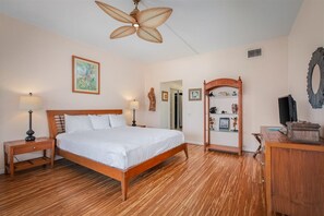 Un dormitorio con una cama de madera, dos mesitas de noche, un ventilador de techo, un aparador de madera y un espejo.