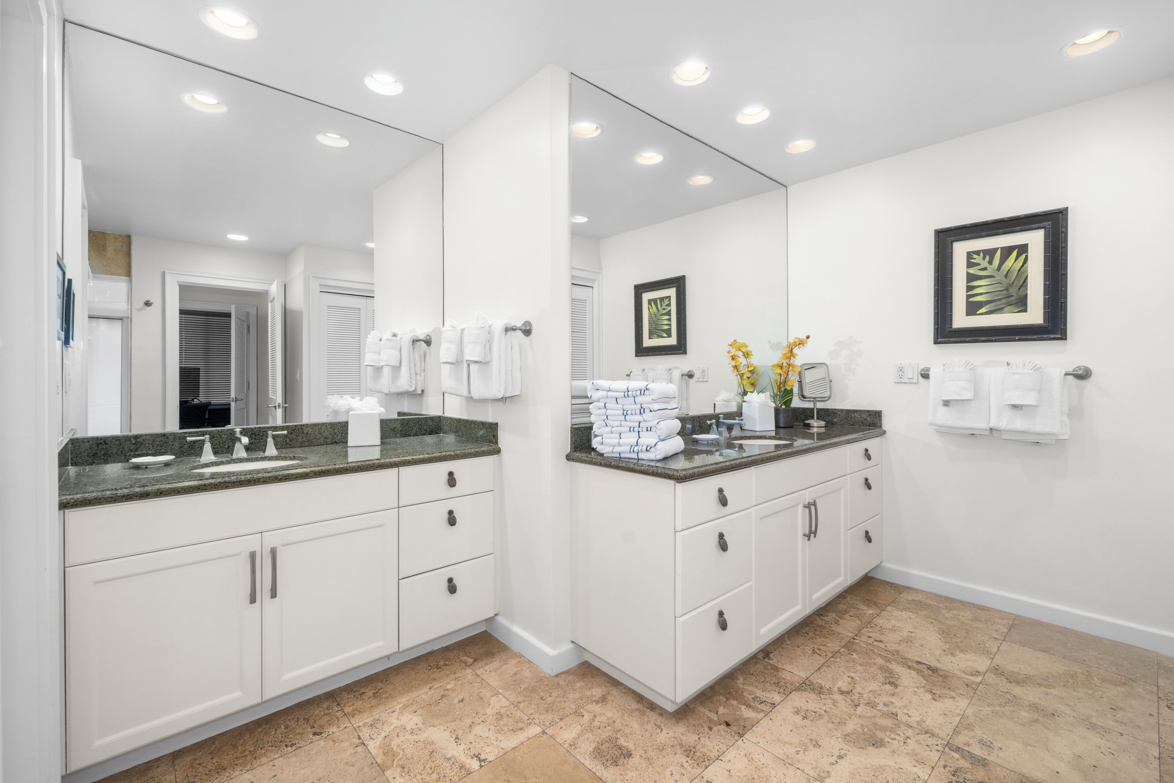 Une salle de bain moderne avec des meubles blancs, un comptoir en granit, un grand miroir et deux tableaux encadrés accrochés au mur.