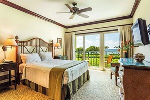 A hotel room with a bed, a desk, a chair, a television, a ceiling fan, and a balcony with a view.