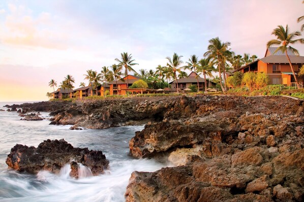 Un resort costero con bungalows sobre el agua, palmeras y una costa rocosa.