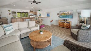 Un amplio espacio habitable con un sofá, una mesa de centro redonda de madera, una mesa de comedor y una zona de cocina con refrigerador y armarios.