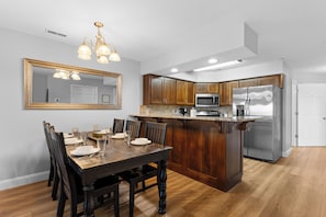 A modern kitchen with wooden cabinetry, a stainless steel refrigerator, and a dining area with a wooden table and chairs.