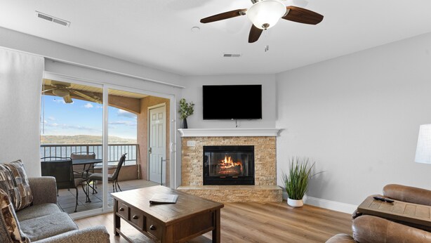Un soggiorno con camino, ventilatore a soffitto, TV e balcone con vista.