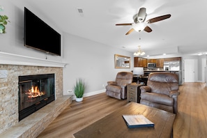 A living room with a fireplace, leather chairs, a flat-screen TV, and a ceiling fan.
