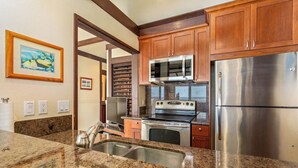 A kitchen with granite countertops, stainless steel appliances, wooden cabinets, and a framed picture on the wall.