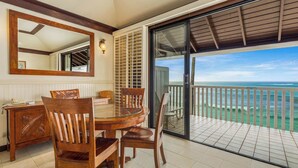 A dining area with a round table and chairs, a wooden cabinet, a mirror, and a view of the ocean through a sliding glass door.