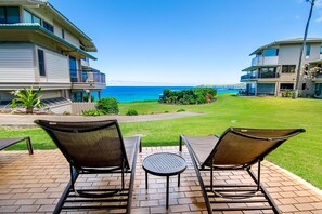 A patio with two chairs and a table, overlooking a grassy area and a building with a balcony.