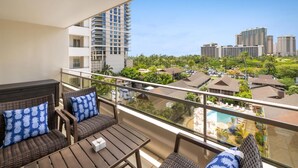 Een balkon met rieten meubilair en uitzicht op een stadsbeeld en een zwembad.