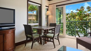 Un balcon avec une table et des chaises pour prendre les repas, un téléviseur posé sur un meuble, et une vue sur un jardin tropical.