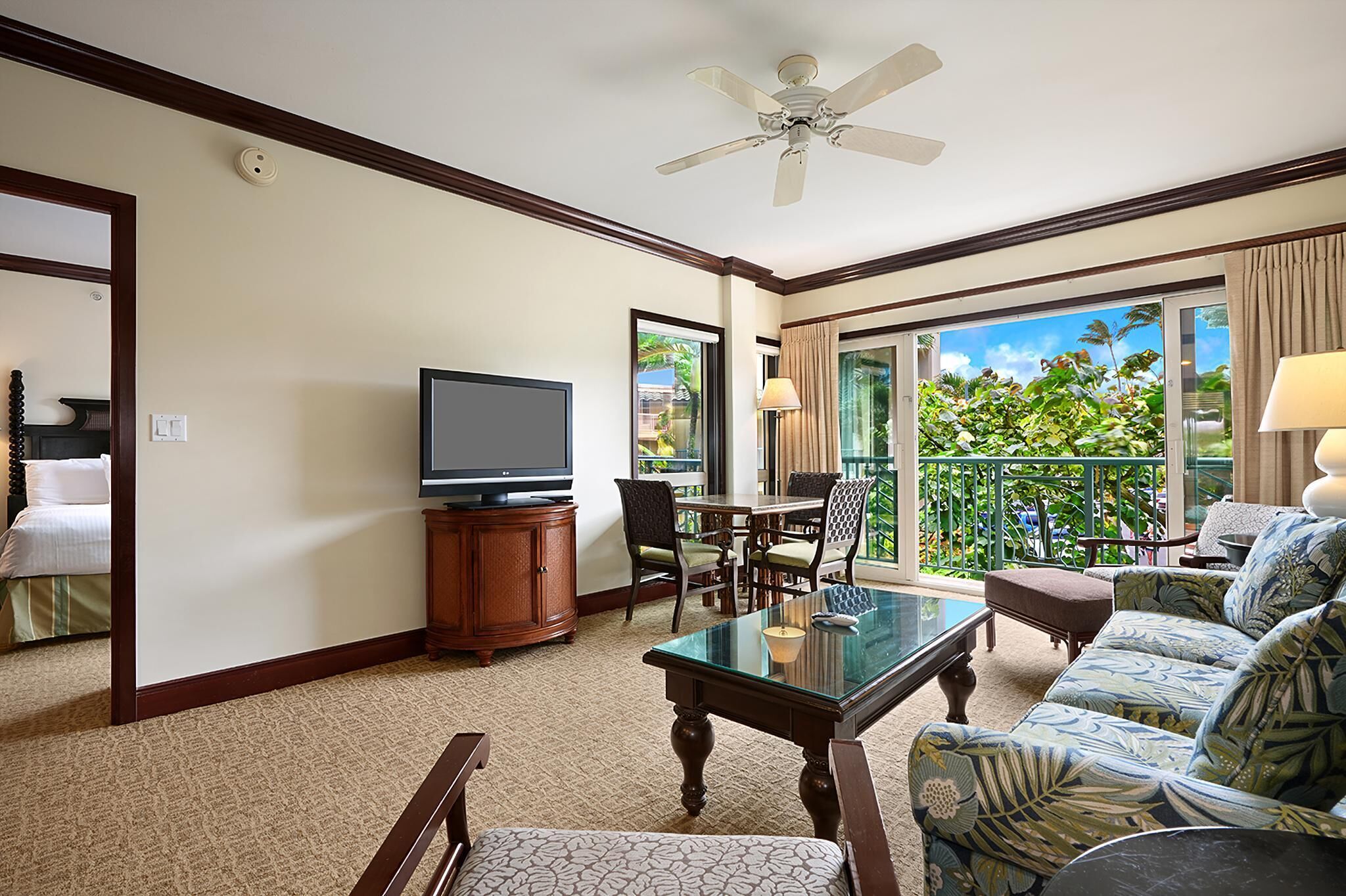 A hotel room with a balcony, a television, a dining table, and a sofa.
