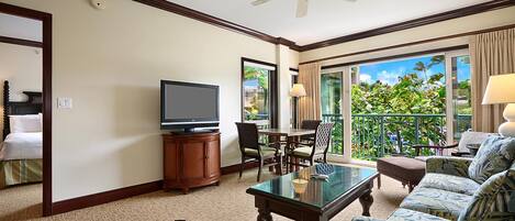A hotel room with a balcony, a television, a dining table, and a sofa.