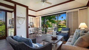 A spacious living area with a dining table, wicker furniture, and a view of a tropical landscape through large sliding doors.