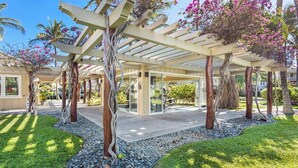 Un espacio al aire libre cubierto con pérgola, árboles y un césped cuidado.