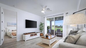 Una sala de estar moderna con un televisor de pantalla plana, un ventilador de techo, un ventanal y vistas al exterior.