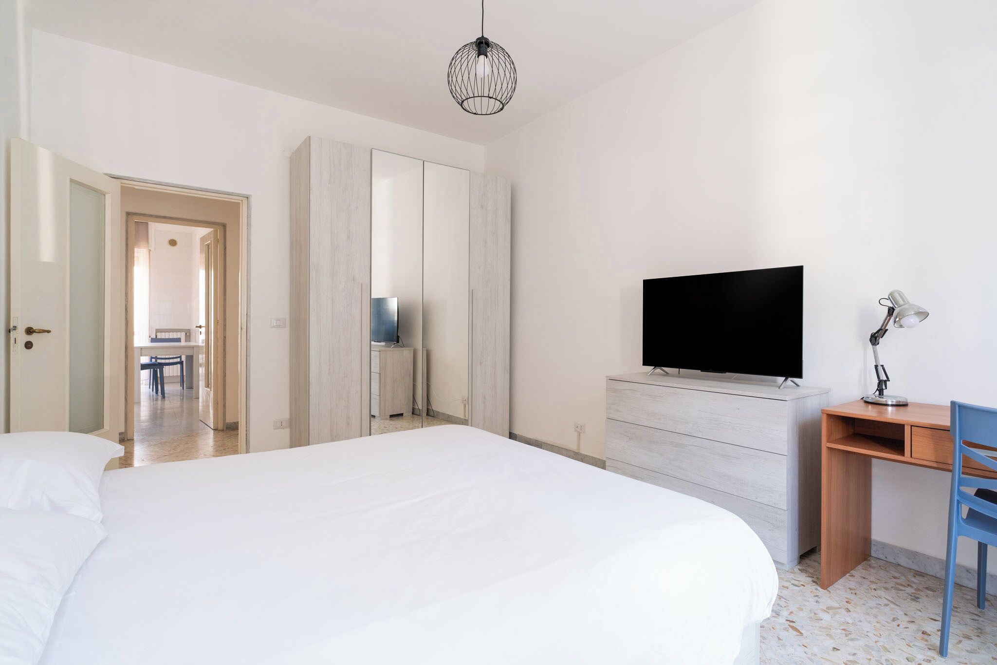 Un dormitorio con cama, escritorio, silla, televisor y armario.