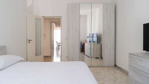 A bedroom with a bed, a wardrobe, a television, and a bathroom visible through an open door. - Appartamento Onda Blu by Wonderful Italy (Bari)