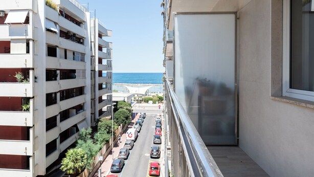 A high-rise building with multiple floors, a balcony with a view of the sea, and a parking lot with cars. - Appartamento Onda Blu by Wonderful Italy (Bari)