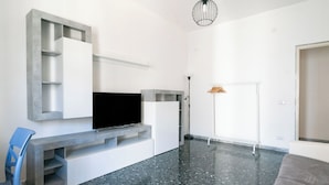 A modern living room with a flat-screen TV, built-in shelving, a blue chair, and a grey sofa. - Appartamento Onda Blu by Wonderful Italy (Bari)