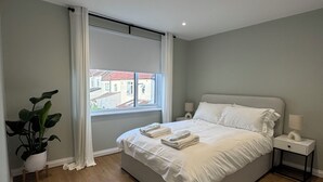 Un dormitorio moderno con una cama grande, una mesita de noche, una planta en maceta y un ventanal con cortinas.