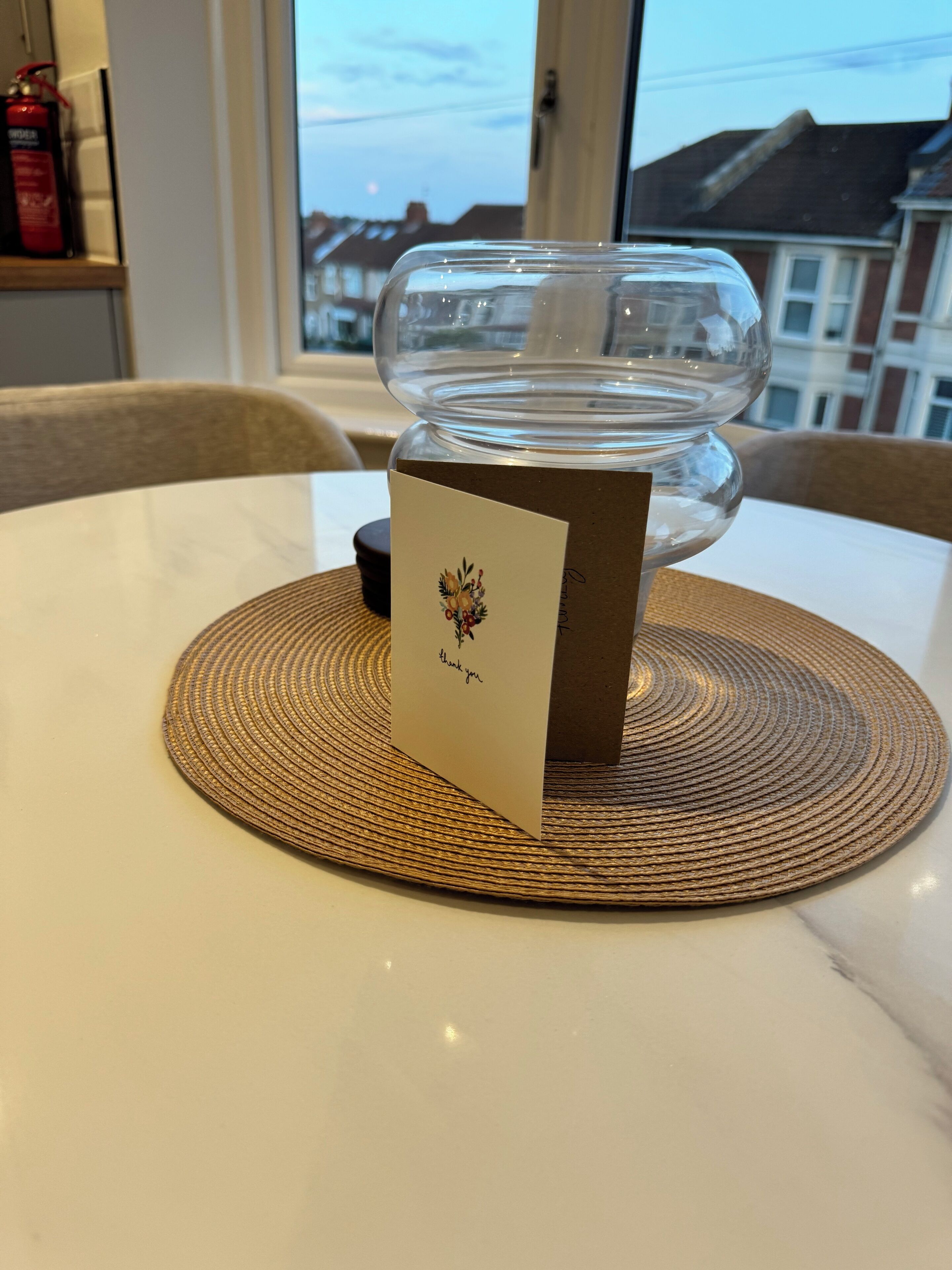Un vase en verre transparent posé sur un set de table en fibres tressées, lui-même placé sur une table.