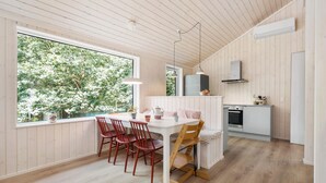 A modern kitchen with wooden paneling, a dining area with red chairs, and a large window overlooking greenery. - 3 bedroom amazing home in Nykøbing Sj (Nykøbing Sj)