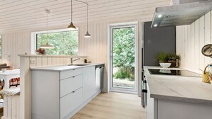 A modern kitchen with a central island, wooden panel walls, and a large window providing a view of greenery. - 3 bedroom amazing home in Nykøbing Sj (Nykøbing Sj)