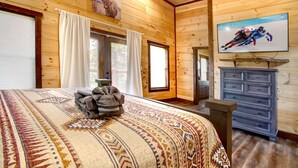 Quarto de cabana de madeira com uma cama grande, um penteado e uma TV fixada na parede.