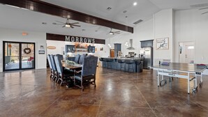 A spacious dining area with a high ceiling, a ping pong table, and a kitchen in the background.