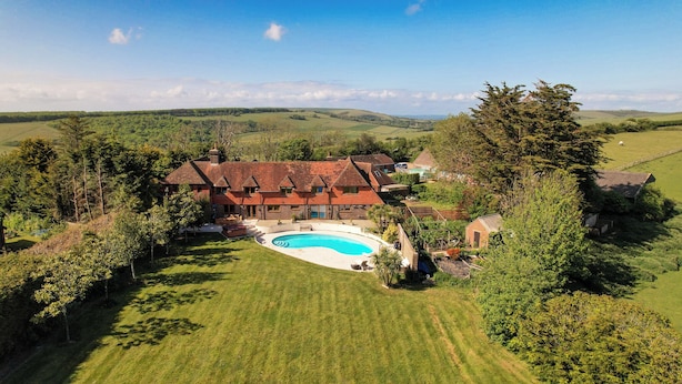 Une grande maison avec une piscine, entourée d’une pelouse bien entretenue et d’arbres.
