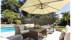 Un espace extérieur aménagé en terrasse, avec des meubles en osier, une piscine et un grand parasol.