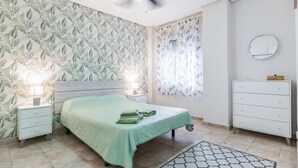 Une chambre à coucher comprenant un lit, des lampes de chevet, une commode, un ventilateur de plafond et une fenêtre avec des rideaux.