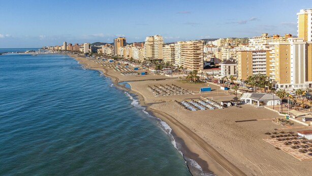 Un paysage urbain côtier avec une plage, des immeubles de grande hauteur et un port de plaisance.