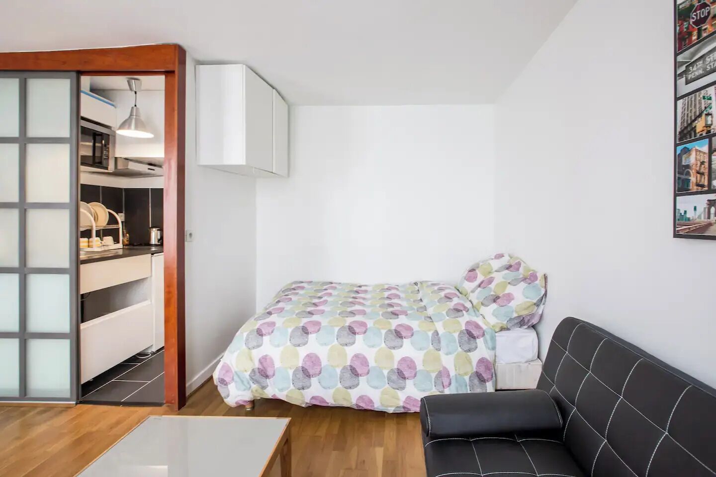Une petite pièce, bien rangée, comprenant un lit, un canapé et un coin cuisine.