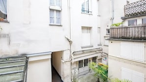 A narrow alleyway between buildings with a small courtyard, a metal gate, and potted plants. - Well-appointed St. Michel studio (Paris)