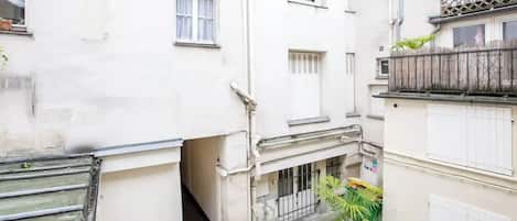 A narrow alleyway between buildings with a small courtyard, a metal gate, and potted plants.