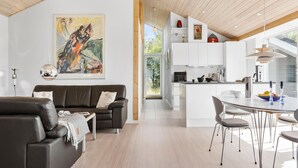 Ein modernes Wohnzimmer mit einem dunkelbraunen Ledersofa, einem Gemälde an der Wand und Blick in den Küchenbereich.