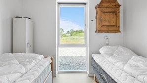 Ein Schlafzimmer mit zwei Betten, einem Holzschrank, einer Tür zu einem Außenbereich und einer Wandleuchte.