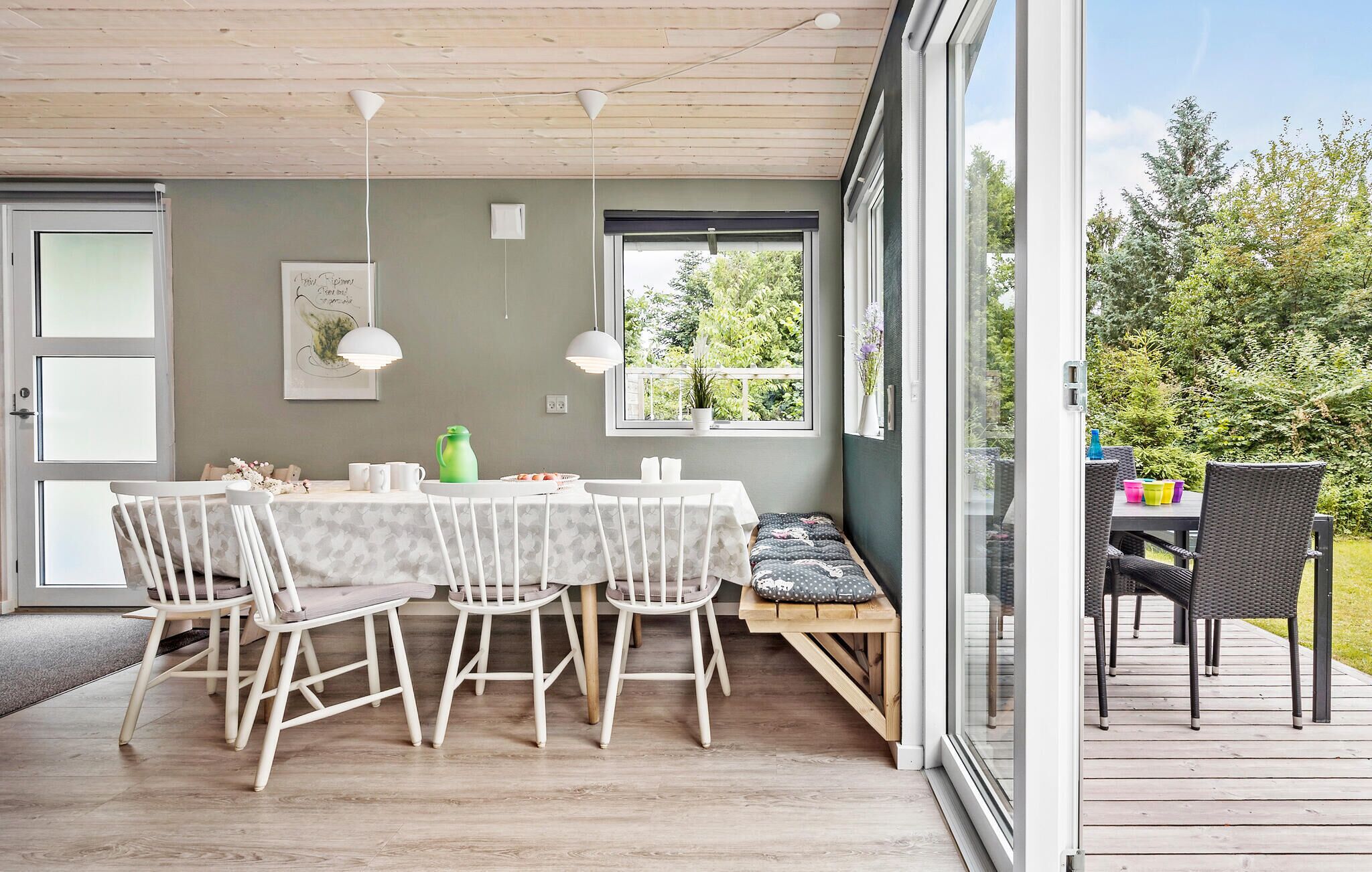 Un comedor con mesa y sillas, un banco y vistas al follaje exterior.