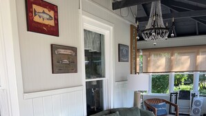 Un sofá tapizado en verde en una habitación con paredes de paneles blancos, una araña y vistas al exterior.