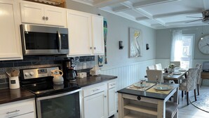 Una cocina moderna con armarios blancos, electrodomésticos de acero inoxidable y una mesa de madera dispuesta para cuatro comensales.