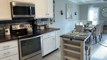 Une cuisine moderne avec des meubles blancs, des appareils en acier inoxydable et une table à manger en bois pour quatre personnes.