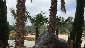 Estátua de bronze de um touro em um jardim com palmeiras e um caminho de cascalho.