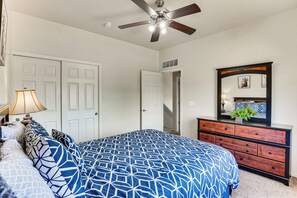 Une chambre à coucher comprenant un lit, une commode, un ventilateur de plafond et une porte donnant sur une autre pièce.