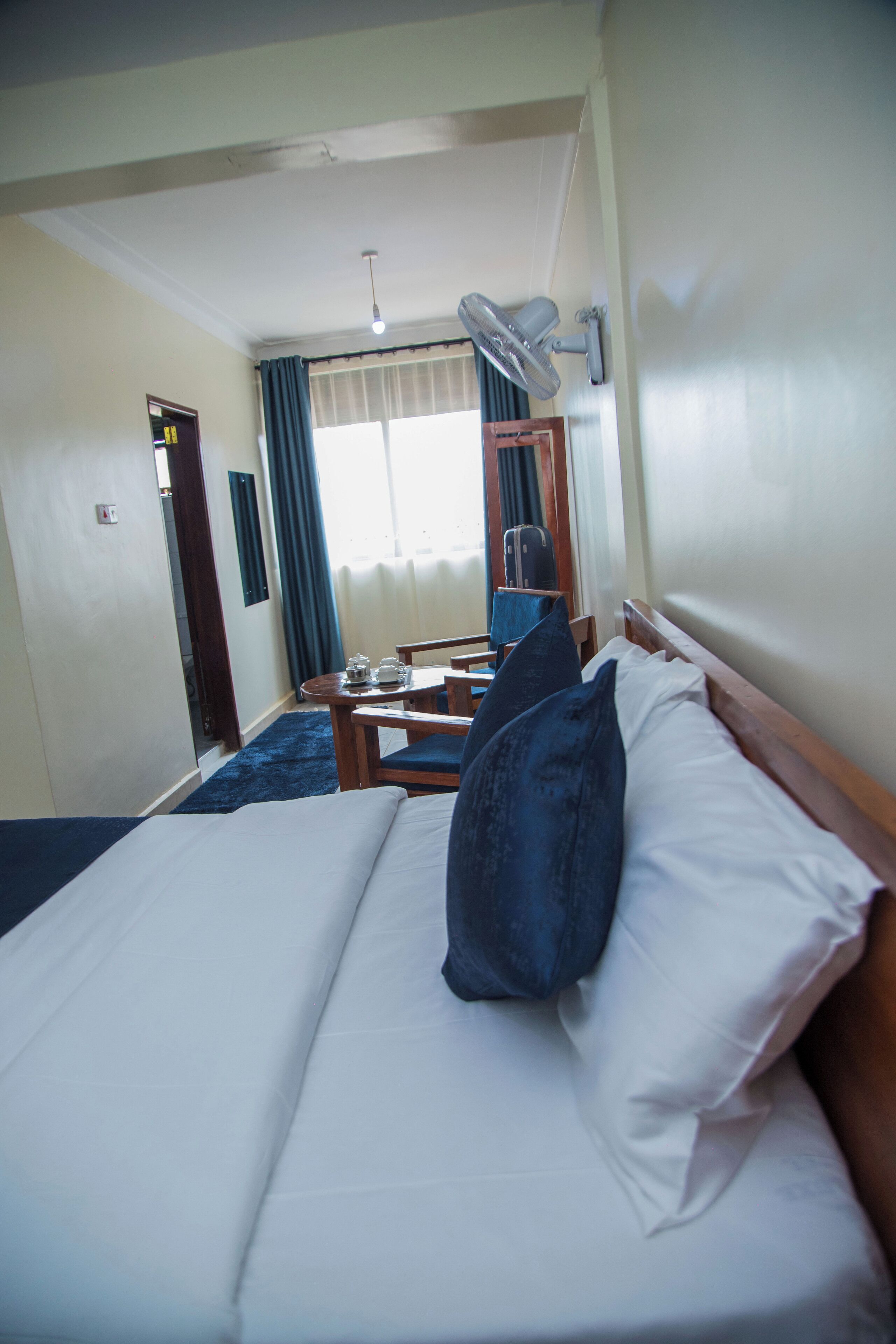 A hotel room with a bed, a desk, a chair, a lamp, and a window with curtains.