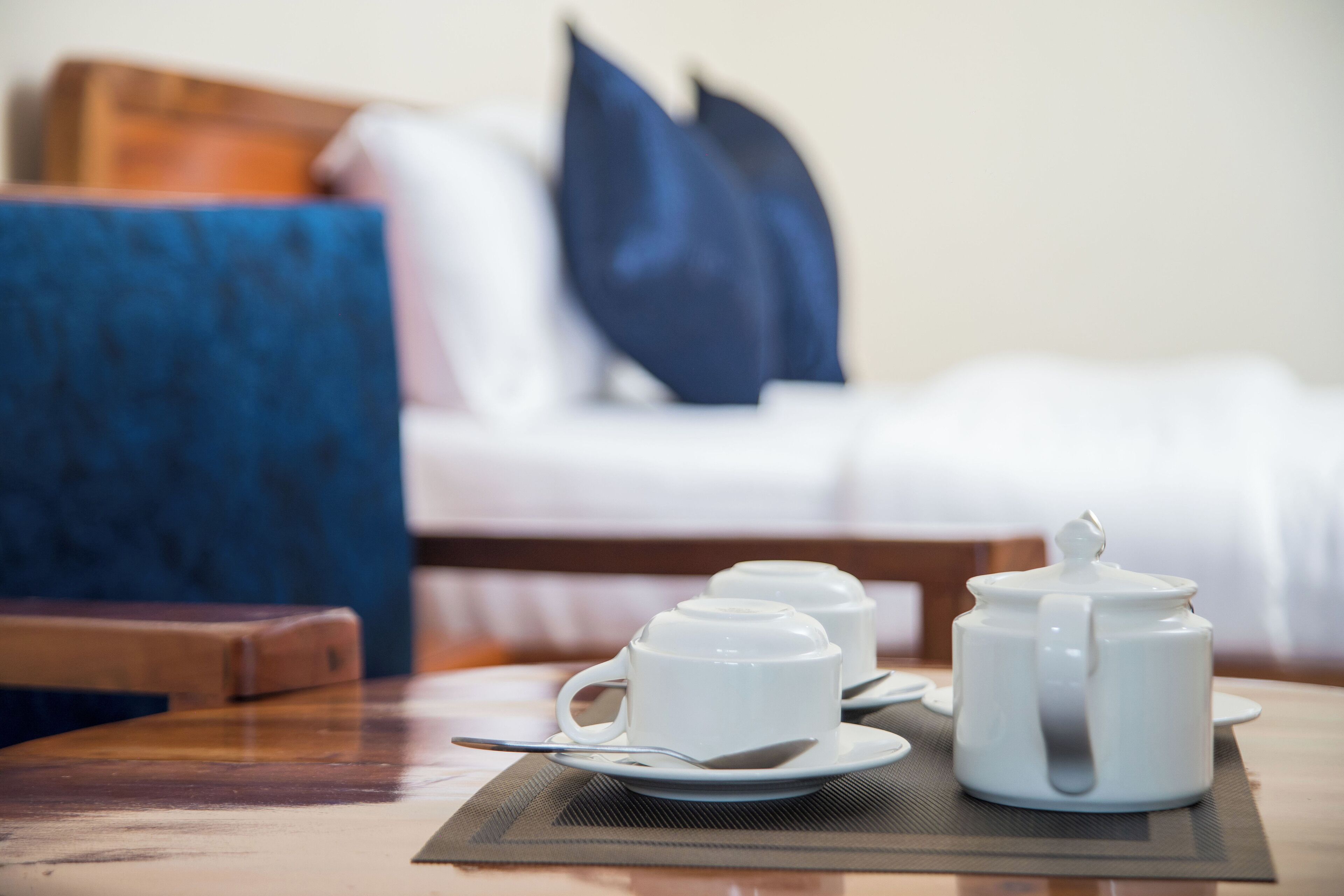 A breakfast setup with a teapot, cups, and a spoon on a table in a hotel room.