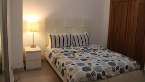 A bedroom with a bed, a nightstand, a lamp, and a wooden wardrobe. - Las Olas 2BR 6PAX 3Bds HugeTerrace (Guayacanes)